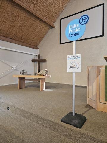 Der schlicht gehaltene Altarbereich der Kirche der Doopsgezinde Gemeente Ouddorp. In der Mitte steht ein Schild "Haltepunkt Leben", das an eine Bushaltestelle erinnert.