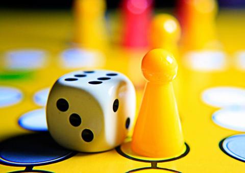 Zwei gelbe Spielfiguren auf einem Mensch ärgere dich nicht-Spielbrett. Daneben ein Würfel, der eine 6 anzeigt.