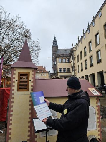 Lorenz Hummel steht vor der Wagenkirche und hält den "Andere Zeiten" Adventskalender in der Hand. Im Hintergrund das Schweinfurter Rathaus.