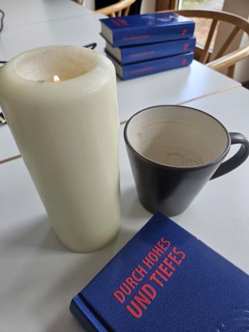 Eine Kerze, eine leere Tasse Kaffee und das Liederbuch "Durch Hohes und Tiefes" auf meinem Besprechungstisch