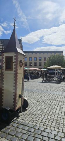 Wagenkirche auf dem Marktplatz, im Hintergrund sitzen Menschen an Cafétischen