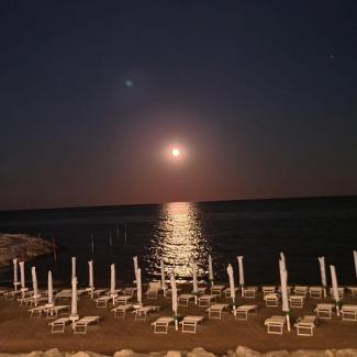 Der Mond scheint über dem Meer. Im Vordergrund am Strand Liegestühle. Kein Mensch ist zu sehen.