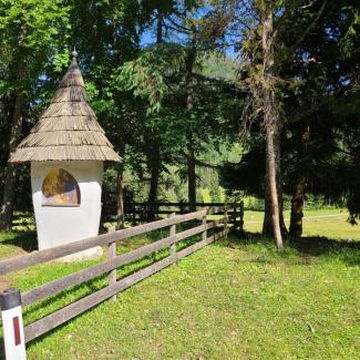 Kleines Marterl mit Strohdach zwischen Bäumen