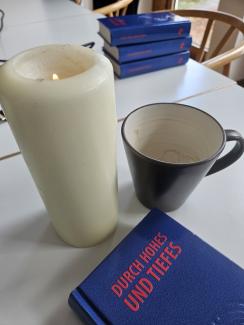 Eine Kerze, eine leere Tasse Kaffee und das Liederbuch "Durch Hohes und Tiefes" auf meinem Besprechungstisch