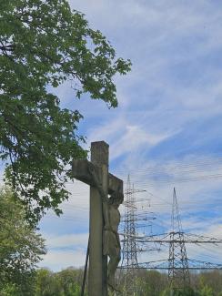 Wegkreuz aus Stein, im Hintergrund Bäume und Hochspannungsleitungen