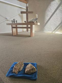 Zwei Mammutzähne liegen auf einem blauen Tuch. Im Hintergrund der schlicht gehaltene Altar der Doopsgezinde Gemeente Ouddorp mit einem großen Holzkreuz dahinter. Von rechts oben fällt Licht auf die Szene.